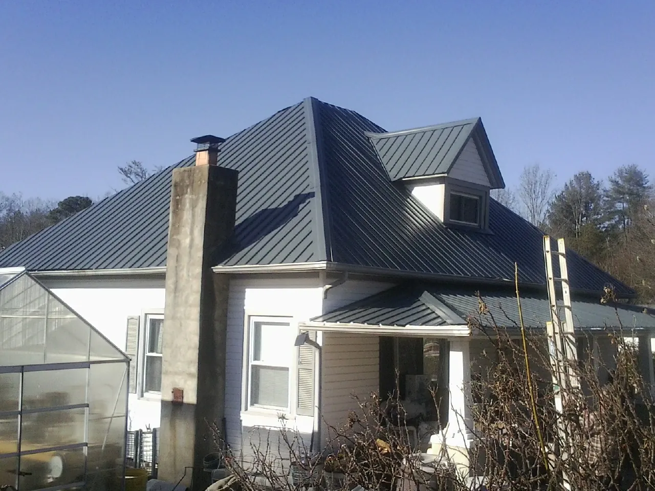 Dark blue standing seam metal roof on a white farmhouse with dormer — Slate & Tile Roof Repair by Roofing Brothers in Spencerport