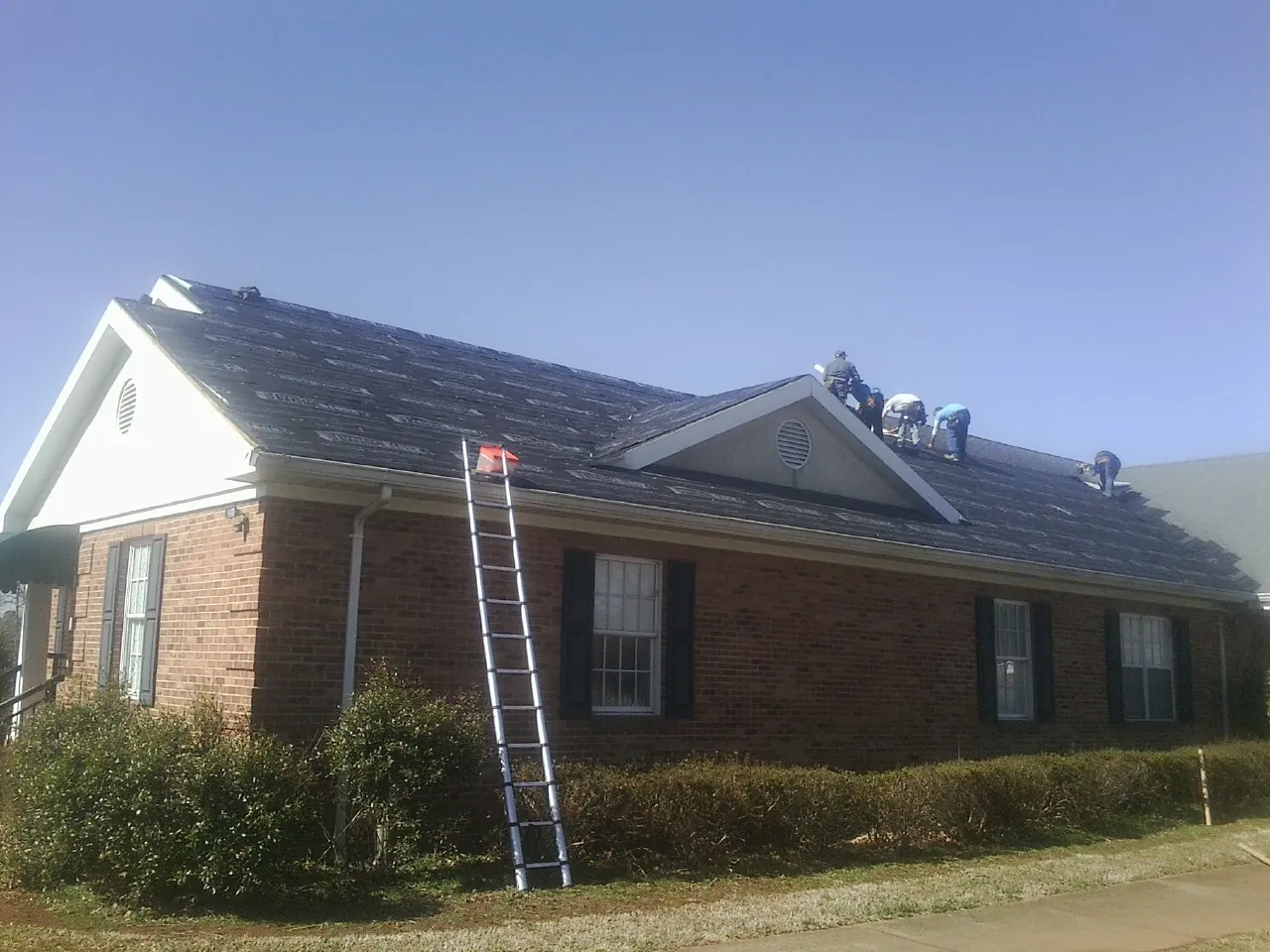 Crew tearing shingles off a brick ranch roof with a ladder set — Emergency Roof Repair work by our crew in Spencerport