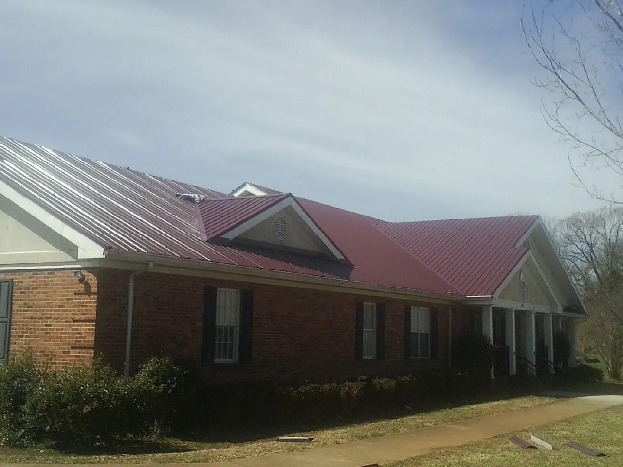 Red metal roof with gabled entries on a long brick building, from a Hail Damage Roof Repair job in Spencerport