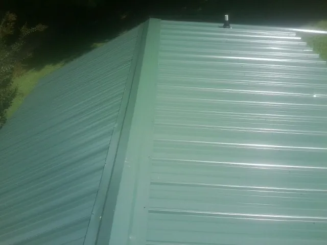 New green metal panels meeting at the ridge of a roof — Flat Roof Repair work by our crew in Spencerport