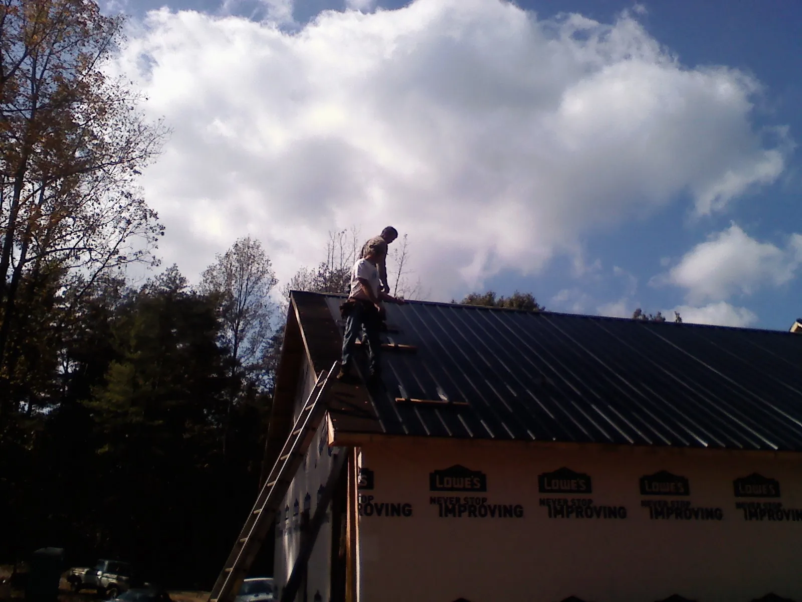 Roofer fastening dark metal panels high against a cloudy sky, from a Roof Inspection job in Spencerport