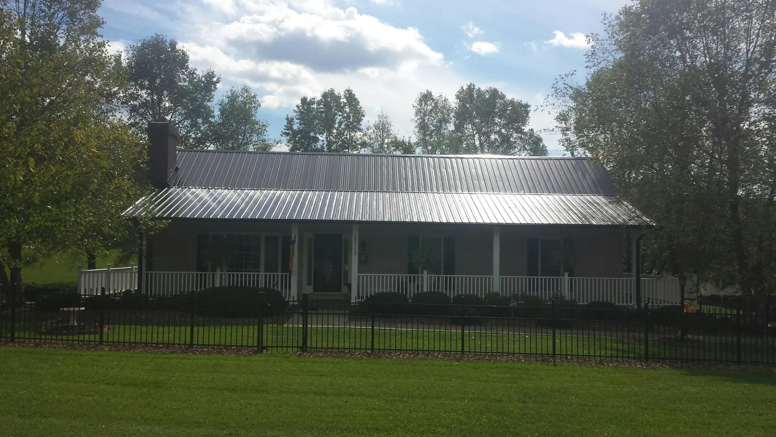 Gray metal roof on a brick ranch with a full width front porch — Gutter Guard Installation work by our crew in Spencerport