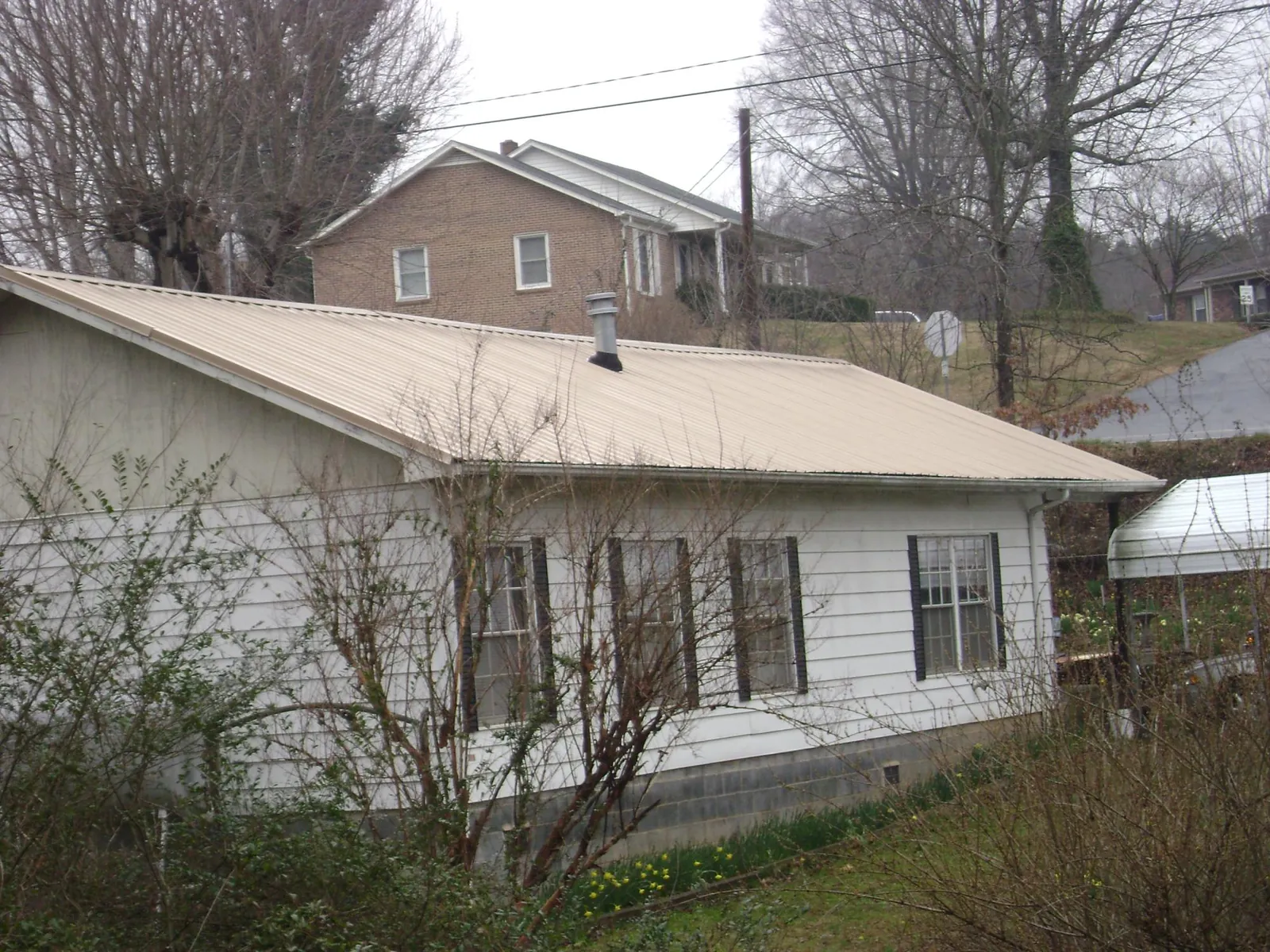 Tan metal roof on a white sided house set into a hillside — Commercial Roofing by Roofing Brothers in Spencerport